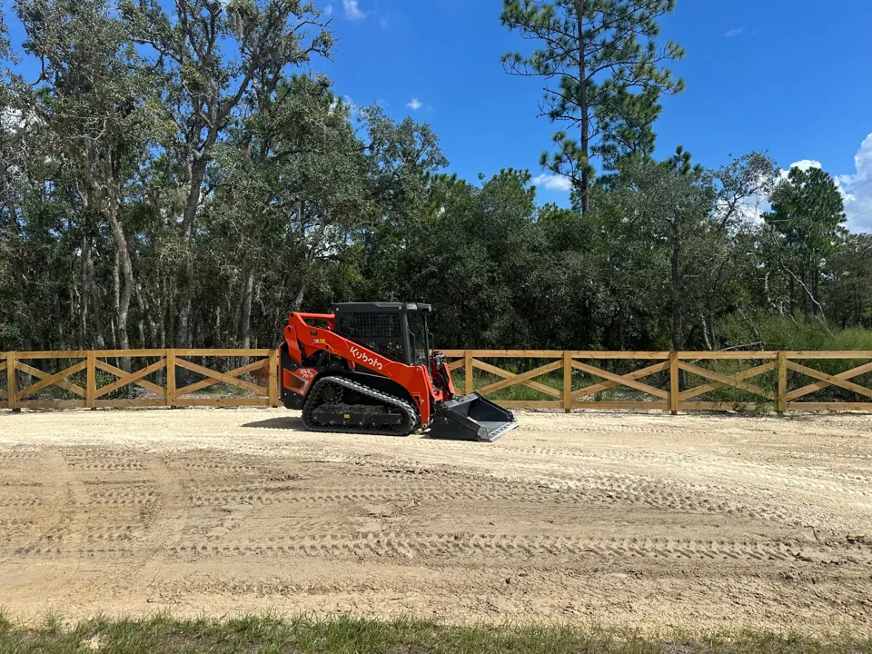 Kubota SVL75-3 spreading and grading road base beside a wooden fence